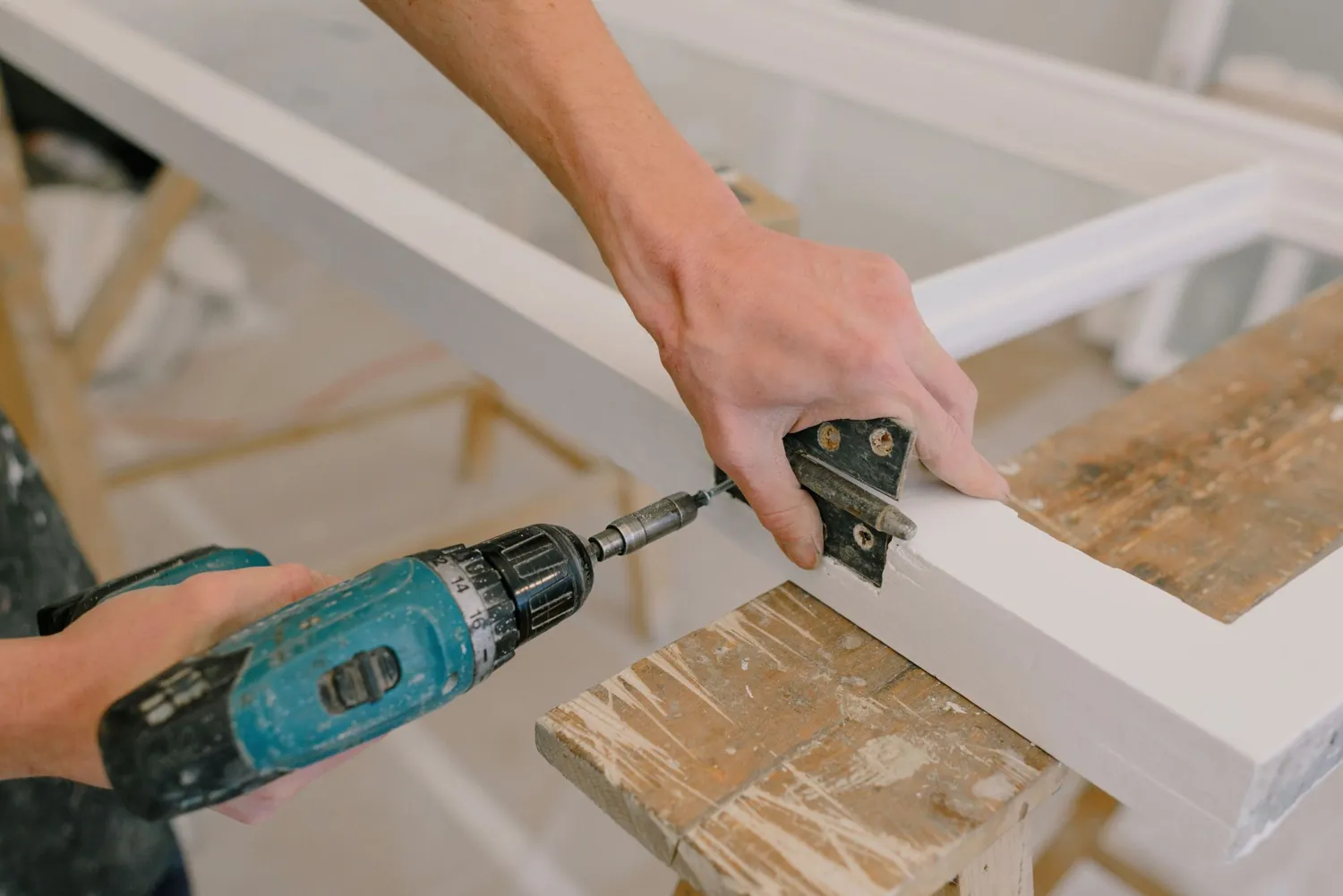 A door hinge being screwed onto a door with a cordless drill
