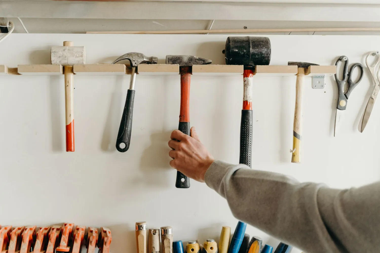 A hand taking a hammer from a wall rack of hand tools